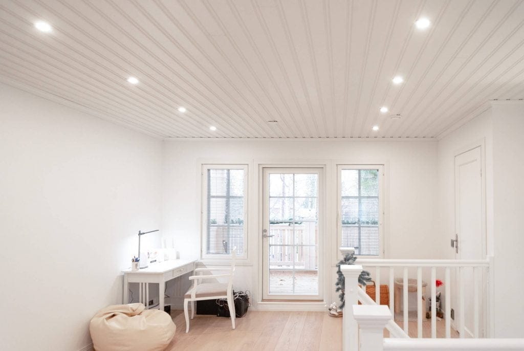 Moderni huone, jossa upotettu LED-valaistus, valkoiset seinät, kirjoituspöytä, tuoli, säkkipussi, lasiovet parvekkeelle; portaiden kaide oikealla.