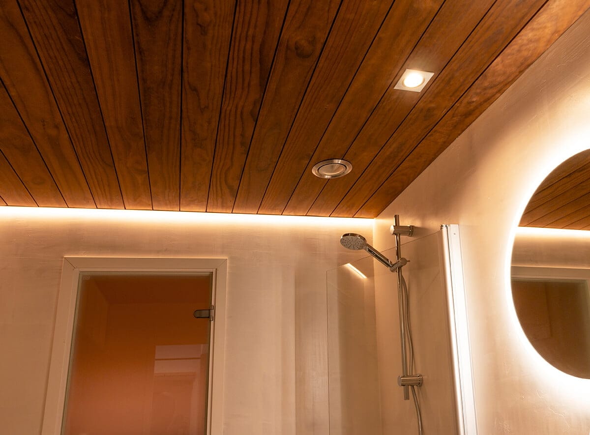 IMG_2902 - LedStore Puinen kattokylpyhuone, jossa ympäristön LED-valaistus, moderni suihkupää, kohdevalo ja pyöreä LED-peili; oviaukko vasemmalla.
