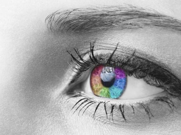 Harmaasävyinen silmän lähikuva, jossa LED-mäinen irisoiva iiris kirkkaissa väreissä: punainen, sininen, vihreä, violetti; terävä kontrasti yksivärisen ihon ja ripsien kanssa.
