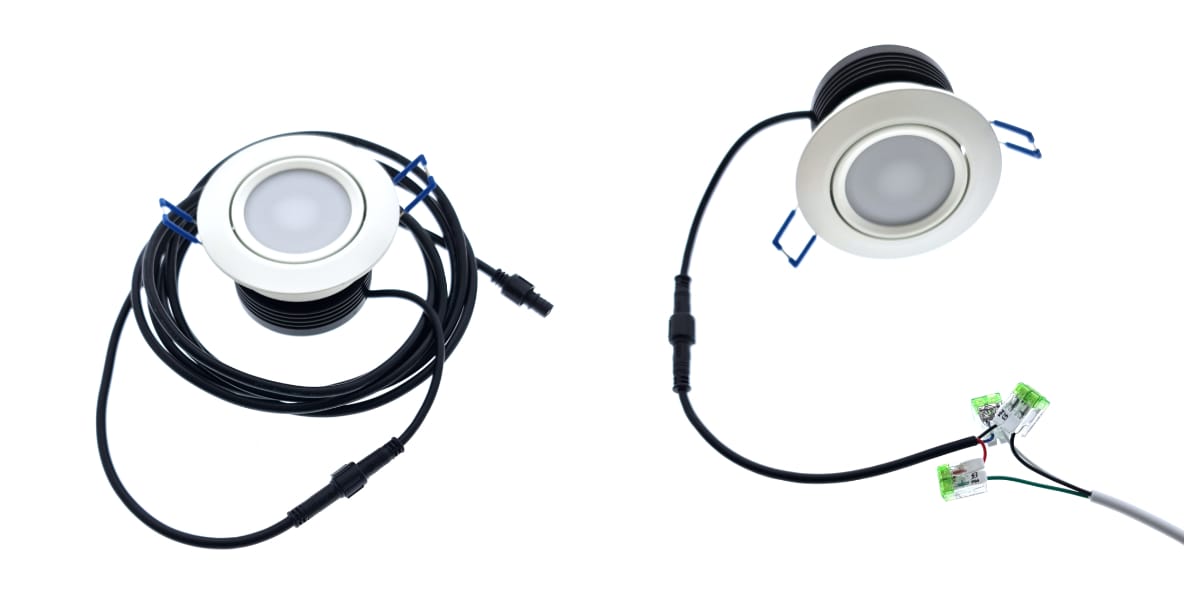 Kaksi pyöreää LED-alasvaloa, joissa on valkoiset kehykset, on kiinnitetty pitkiin mustiin johtoihin. Valoissa on liittimet johtojen päissä. Toinen johto on kierretty, kun taas toinen ulottuu ja yhdistyy vihreisiin riviliittimiin korostaen oman tyylikkään LED-integraatiota.